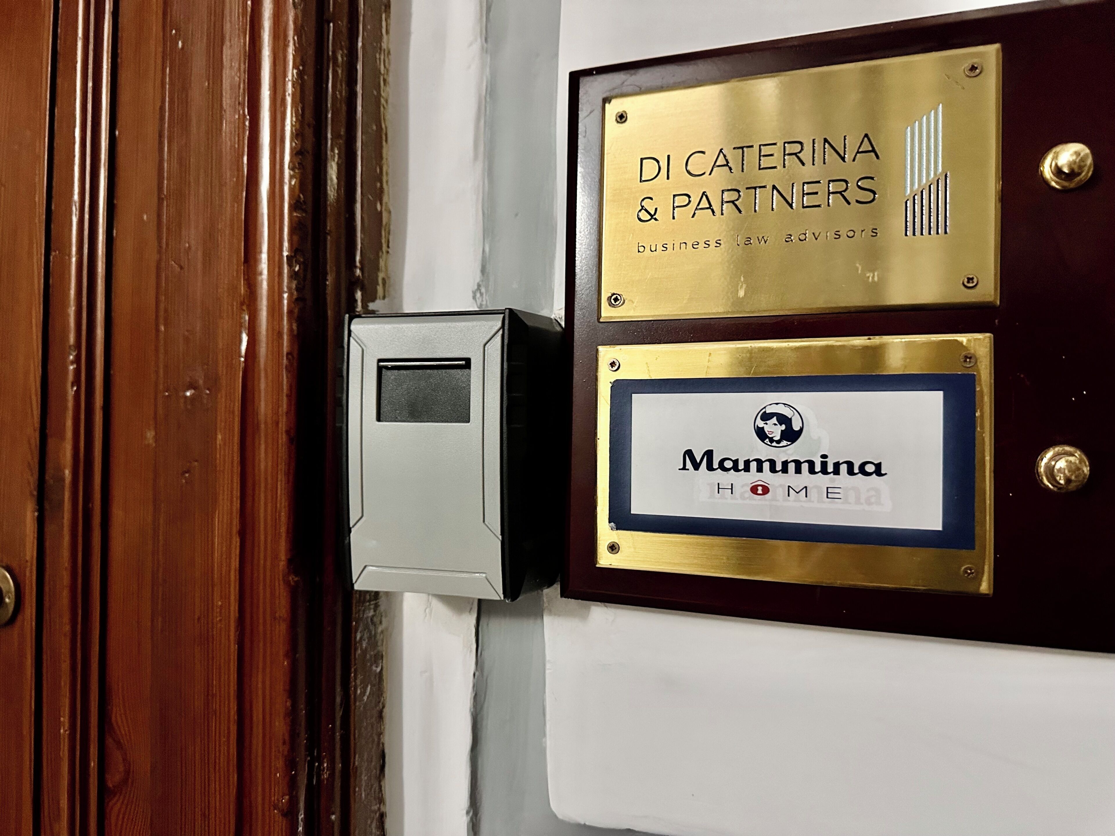 A door with a brass plaque reading "DI CATERINA & PARTNERS business law advisors" and another plaque with "Mammina HOME".