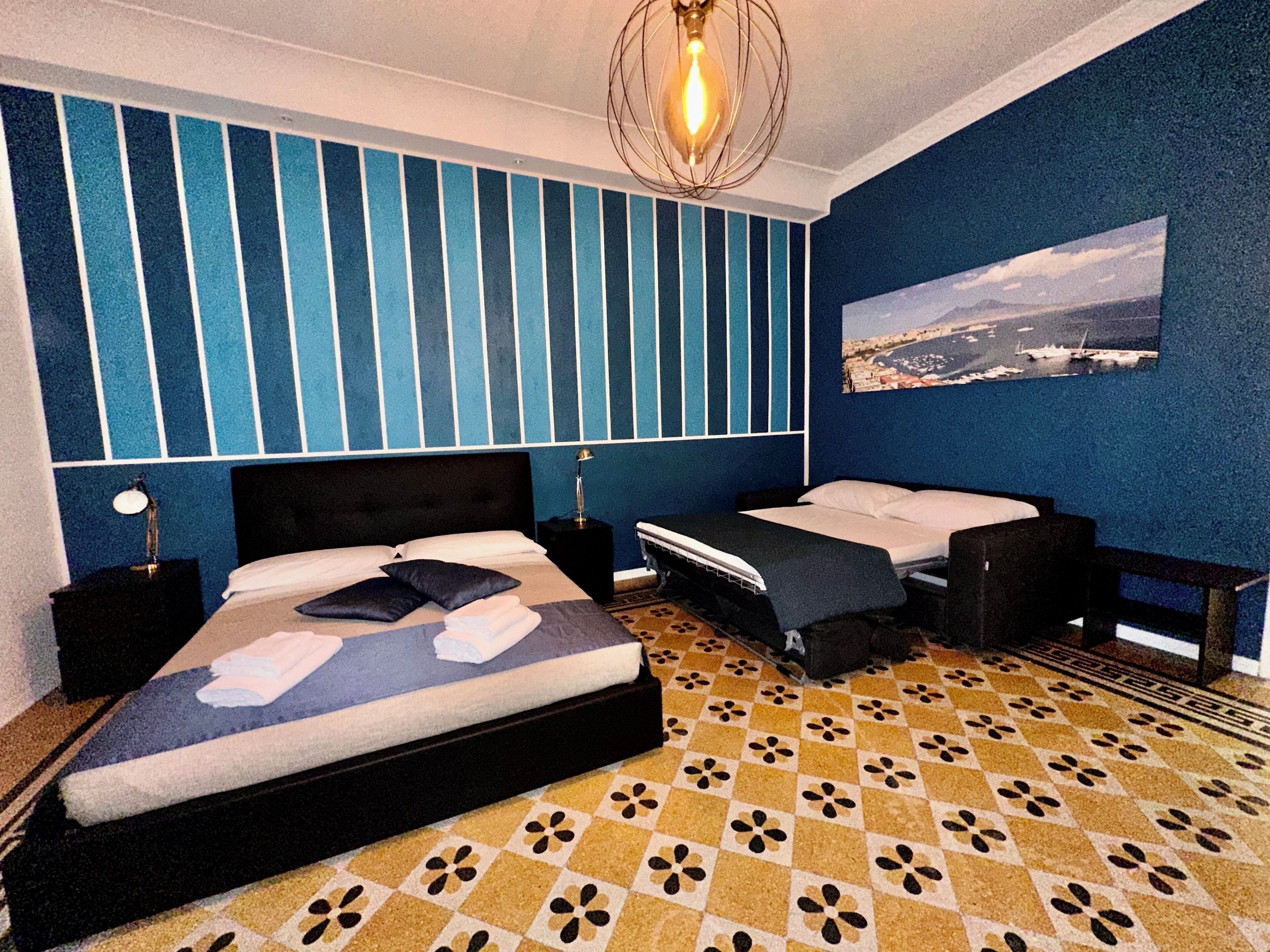 A room with two beds, a patterned floor, a cityscape painting, and a unique ceiling light.