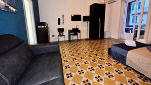 A modern hotel room with a checkered floor, a sofa, a bed, a desk, and a view of the city. - Mammina Home Napoli - Santa Lucia (Naples)