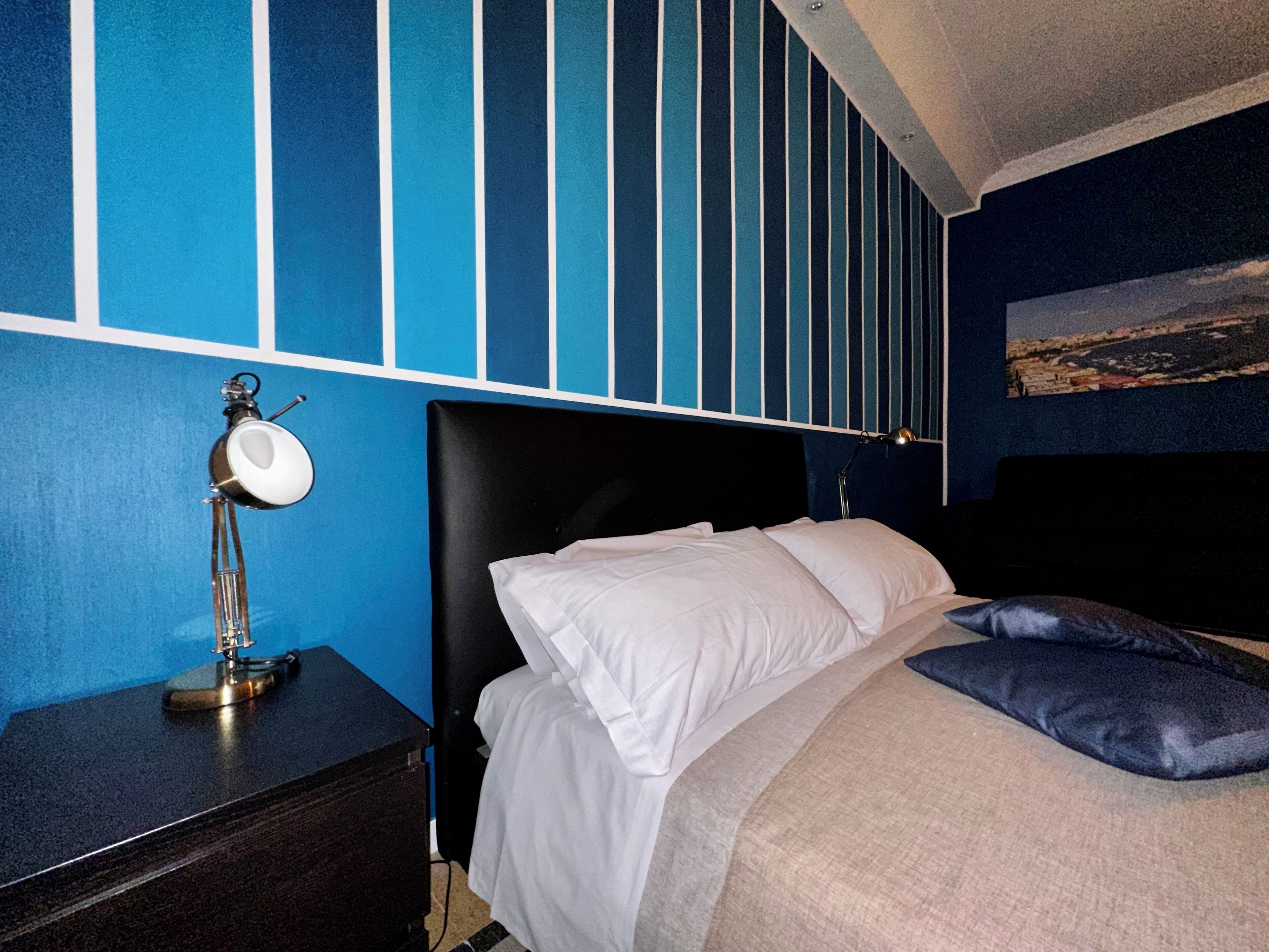 A hotel room with a bed, a nightstand, a lamp, and a painting on the wall.