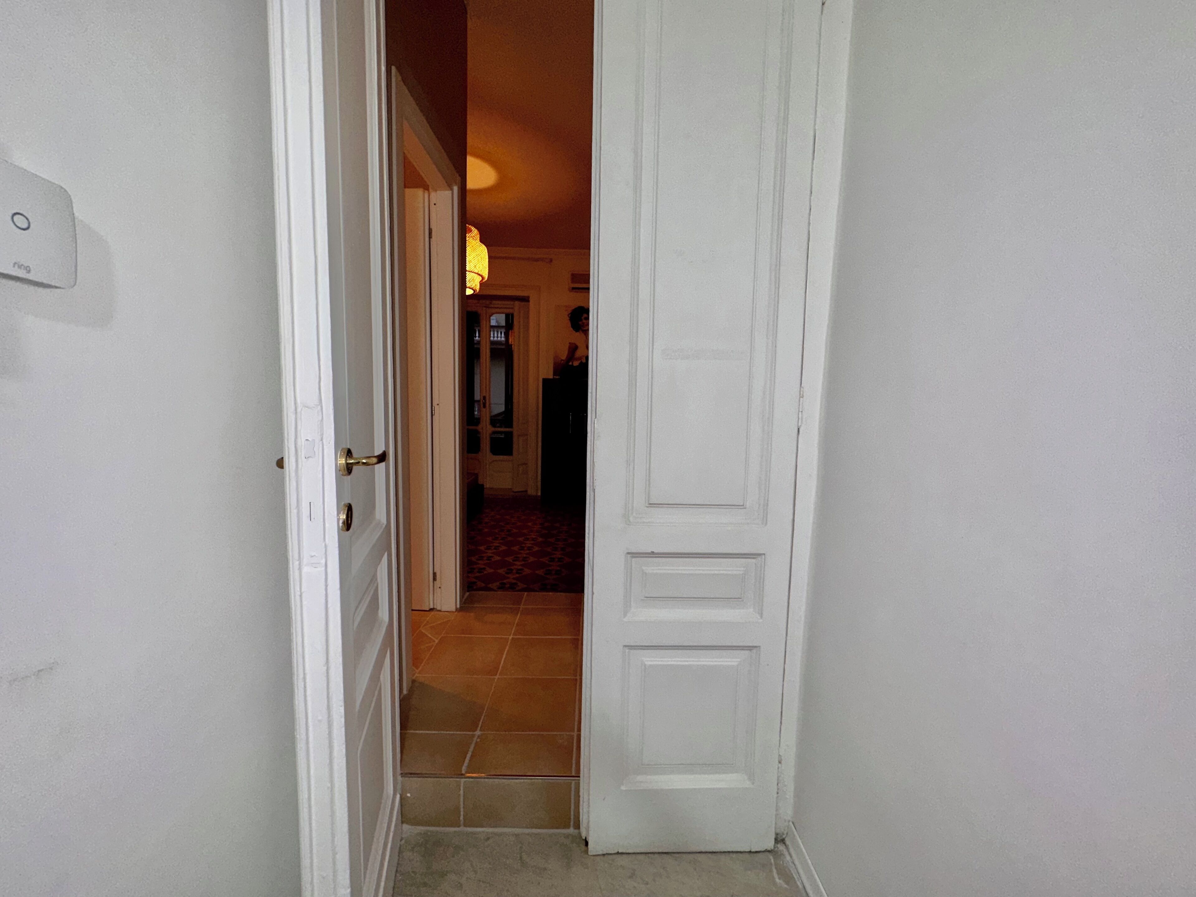 Un pasillo con una puerta blanca que da a una habitación con piso de baldosas.