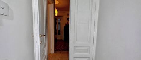 Un pasillo con una puerta blanca que da a una habitación con piso de baldosas.