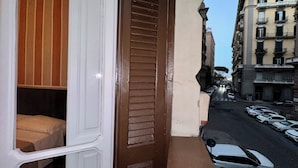 A narrow balcony with a bed and a view of parked cars and buildings. - Mammina Home Napoli - Santa Lucia (Naples)