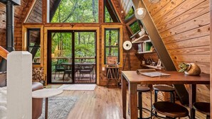 A cabin with a loft bedroom, a dining area, and a large sliding glass door leading to an outdoor deck. - NEW! Creekside Ranch A-Frame (Young Harris)