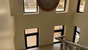 A staircase with a metal handrail, a circular mirror with a wooden frame, and multiple windows with a view of the outside. - Kampala (Kampala)