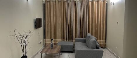 Una sala de estar con un sofá gris, una mesa de centro de madera y un florero negro con ramas.