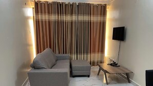 A living room with a sofa, ottoman, and a small table with a lamp and phone. - Kampala (Kampala)