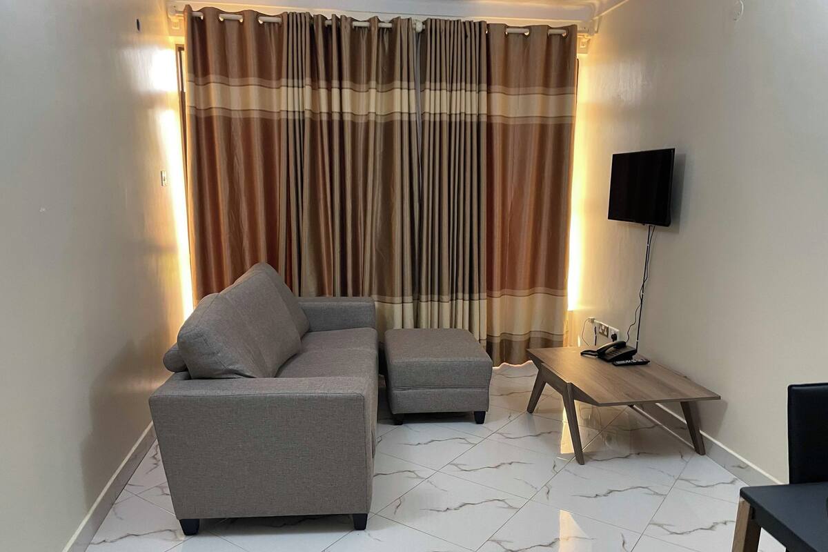 Ein Wohnzimmer mit einer Couch, einem Hocker und einem kleinen Tisch mit Lampe und Telefon.