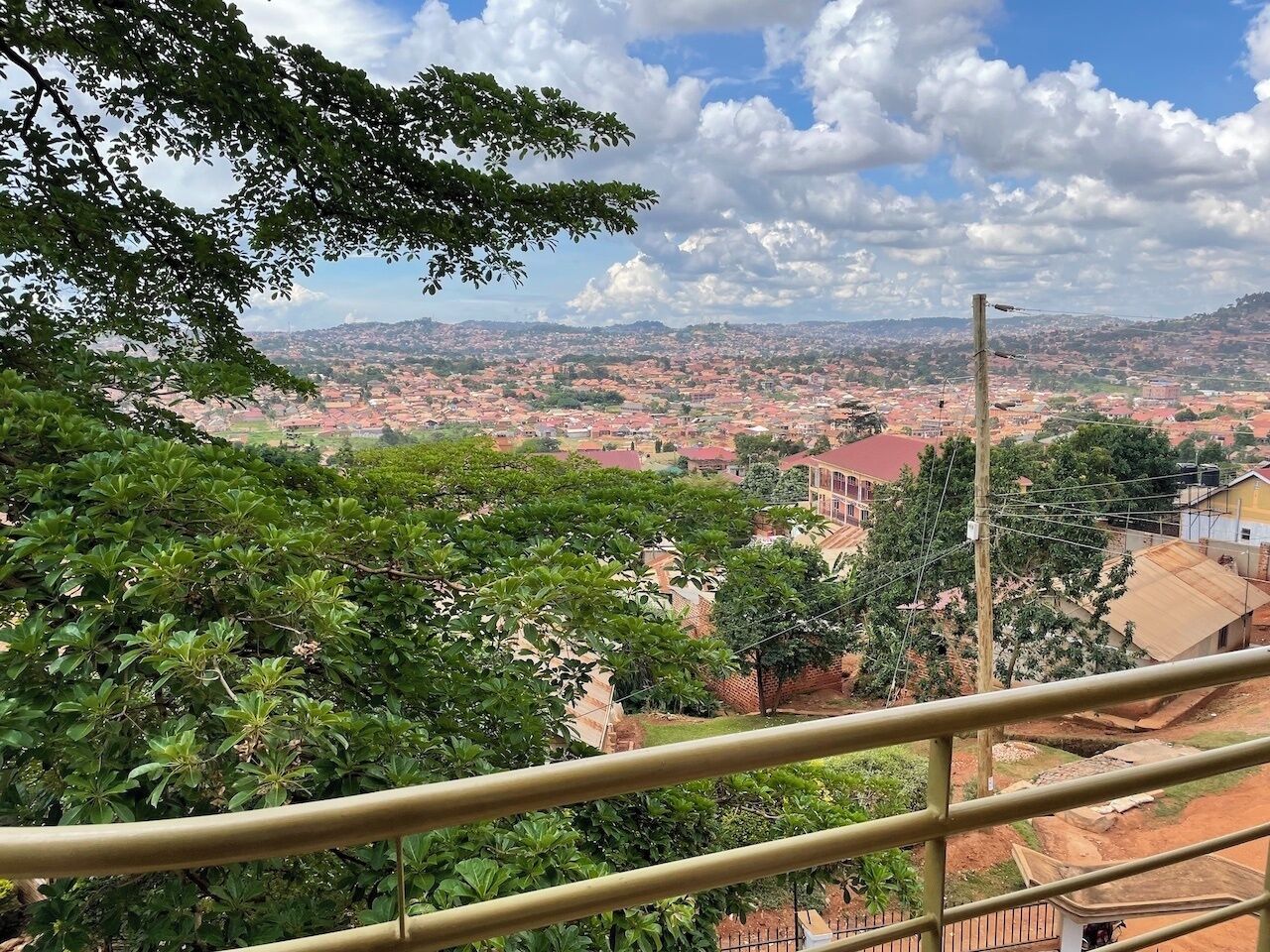 A balcony with a view of a cityscape, including buildings and greenery.