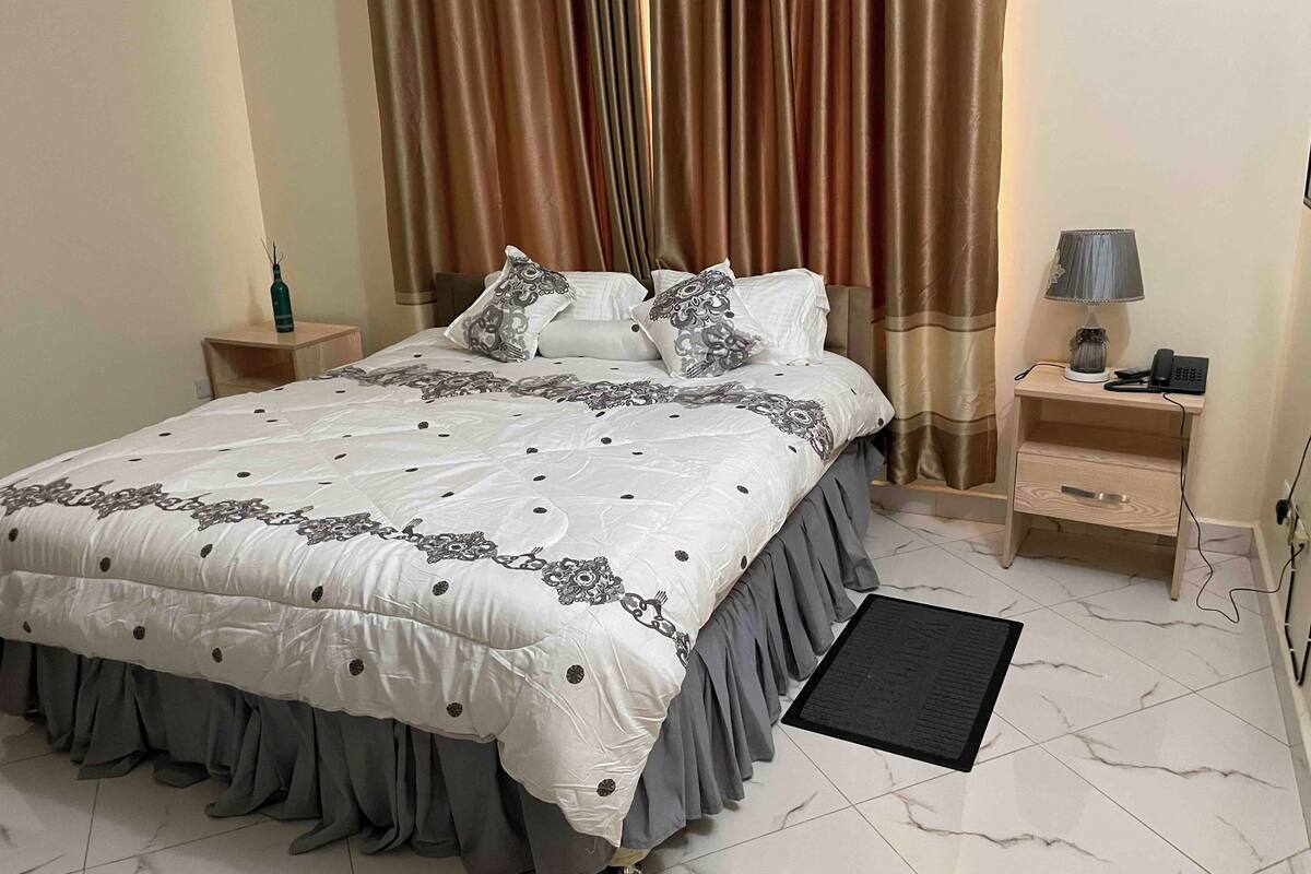 Ein ordentlich eingerichtetes Schlafzimmer mit einem großen Bett, zwei Nachttischen, einem Schreibtisch mit Lampe und einem Telefon.
