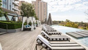 A rooftop pool area with lounge chairs, umbrellas, and a view of surrounding buildings. - The Capital on Park Apart-hotel (Sandton)