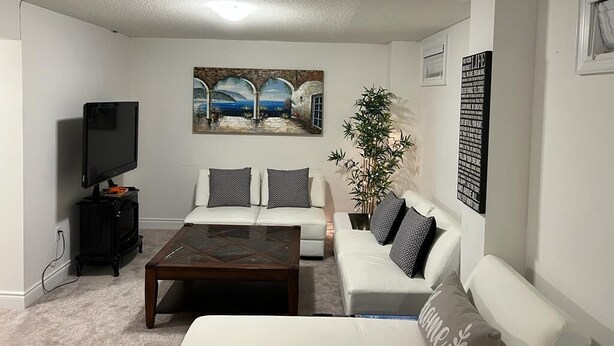 Una sala de estar con un sofá blanco, una mesa de centro, un televisor y un cuadro en la pared.