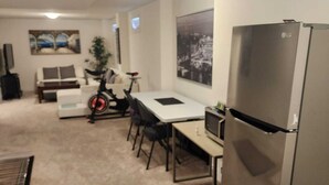 Un espacio habitable compacto con kitchenette, una zona de comedor con mesa y sillas, un pequeño sofá, una bicicleta y un refrigerador.