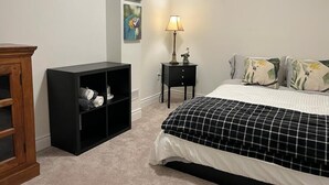Un dormitorio con una cama, un estante negro, una mesita de noche con lámpara y decoración en la pared.