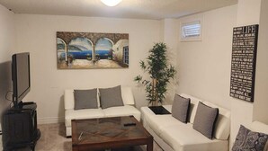 Sala de estar con un sofá blanco, una mesa de centro, un televisor y un cuadro de una escena costera.