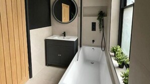 Une salle de bain moderne avec une baignoire sur pieds, un miroir rond, un petit lavabo et une plante en pot.