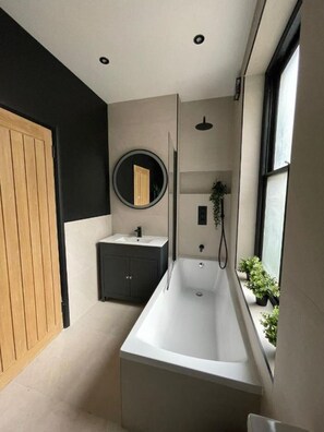 Bathroom features a large bathtub, round mirror, and small window.