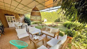 A patio area with a wooden sofa set, a turquoise chair, and a hanging basket. - Villa Julien (Gassin)