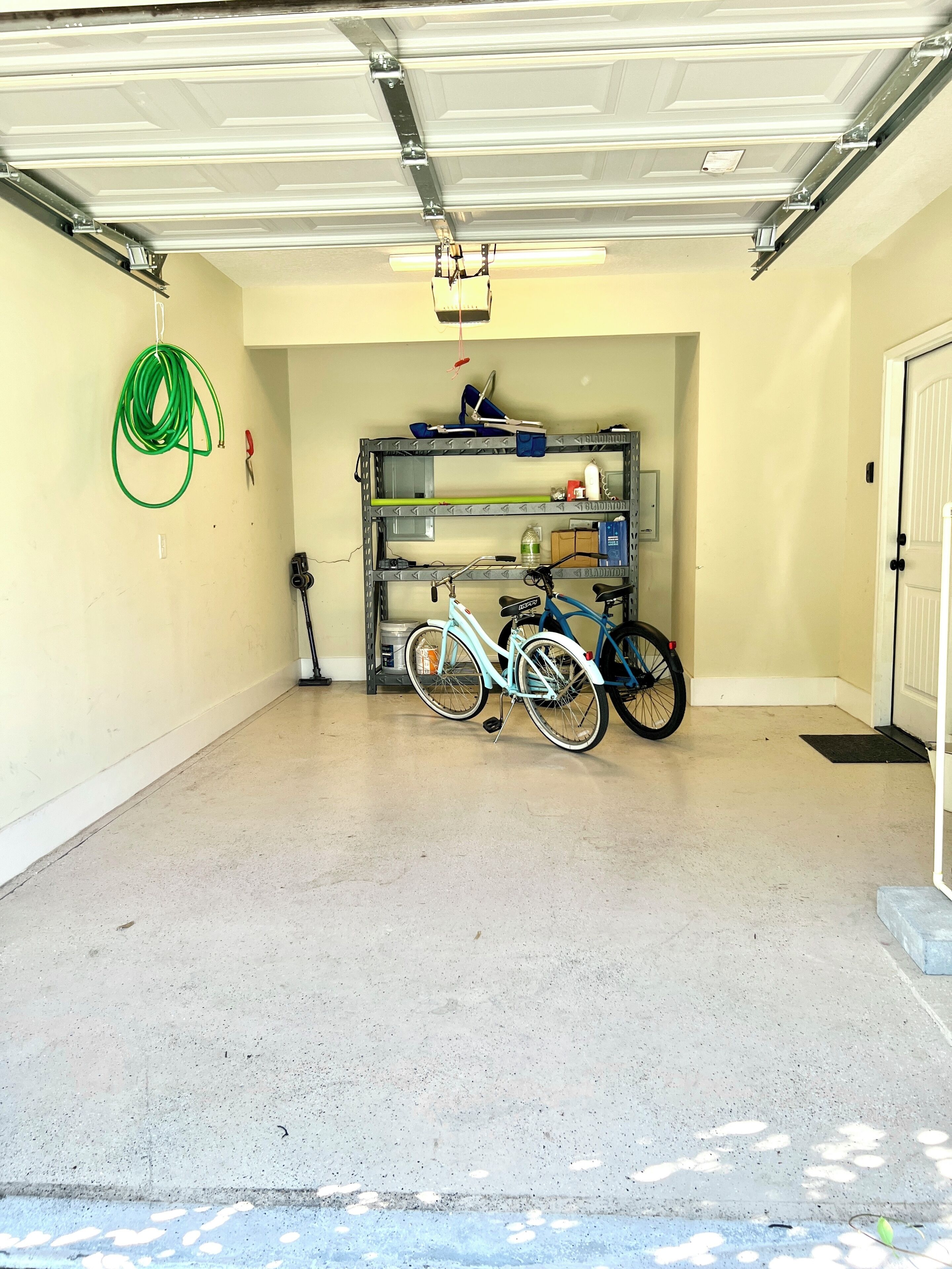 Een garage met een fiets, een metalen plank en een groene tuinslang.