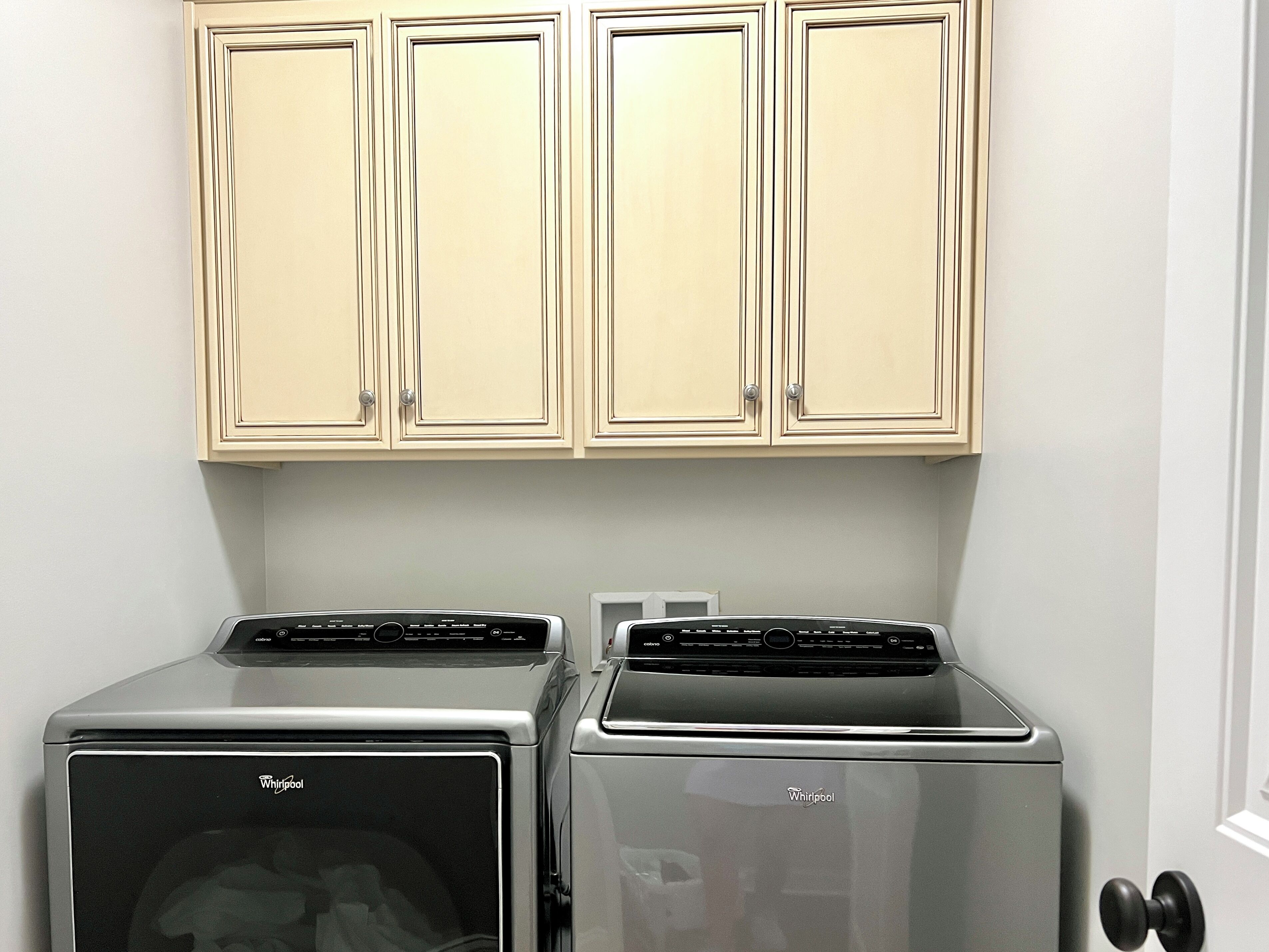 Two Whirlpool appliances in a kitchen with cream-colored cabinets and a white door.