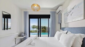 A modern hotel room with a large bed, a balcony with a view, a hanging light fixture, and a painting on the wall. - Uranos - Two Bedroom Villa, Sleeps 4 (Corfu)