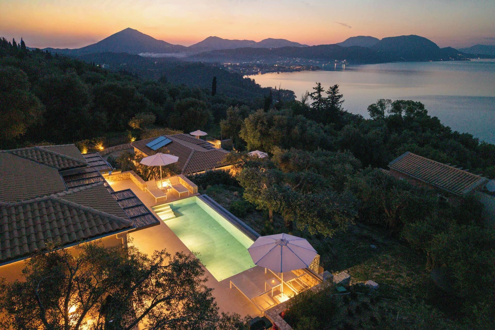 A resort with a swimming pool, outdoor seating, and a view of a lake and mountains.