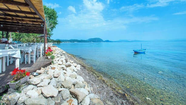 A seaside restaurant with outdoor seating, a rocky shoreline, and a clear view of the sea and distant hills. - Uranos - Two Bedroom Villa, Sleeps 4 (Corfu)