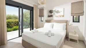 Un dormitorio moderno con una cama grande, una mesita de noche, una lámpara de pared y vistas a la vegetación a través de una puerta corredera.