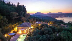 Una villa en la ladera con piscina, rodeada de bosque denso y vistas a un lago.