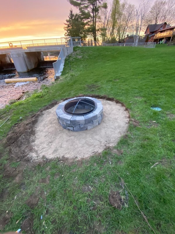 A circular stone fire pit in a grassy area with a concrete structure in the background.