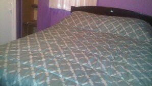Un letto con copriletto decorato in una stanza con pareti viola e una porta visibile sullo sfondo.