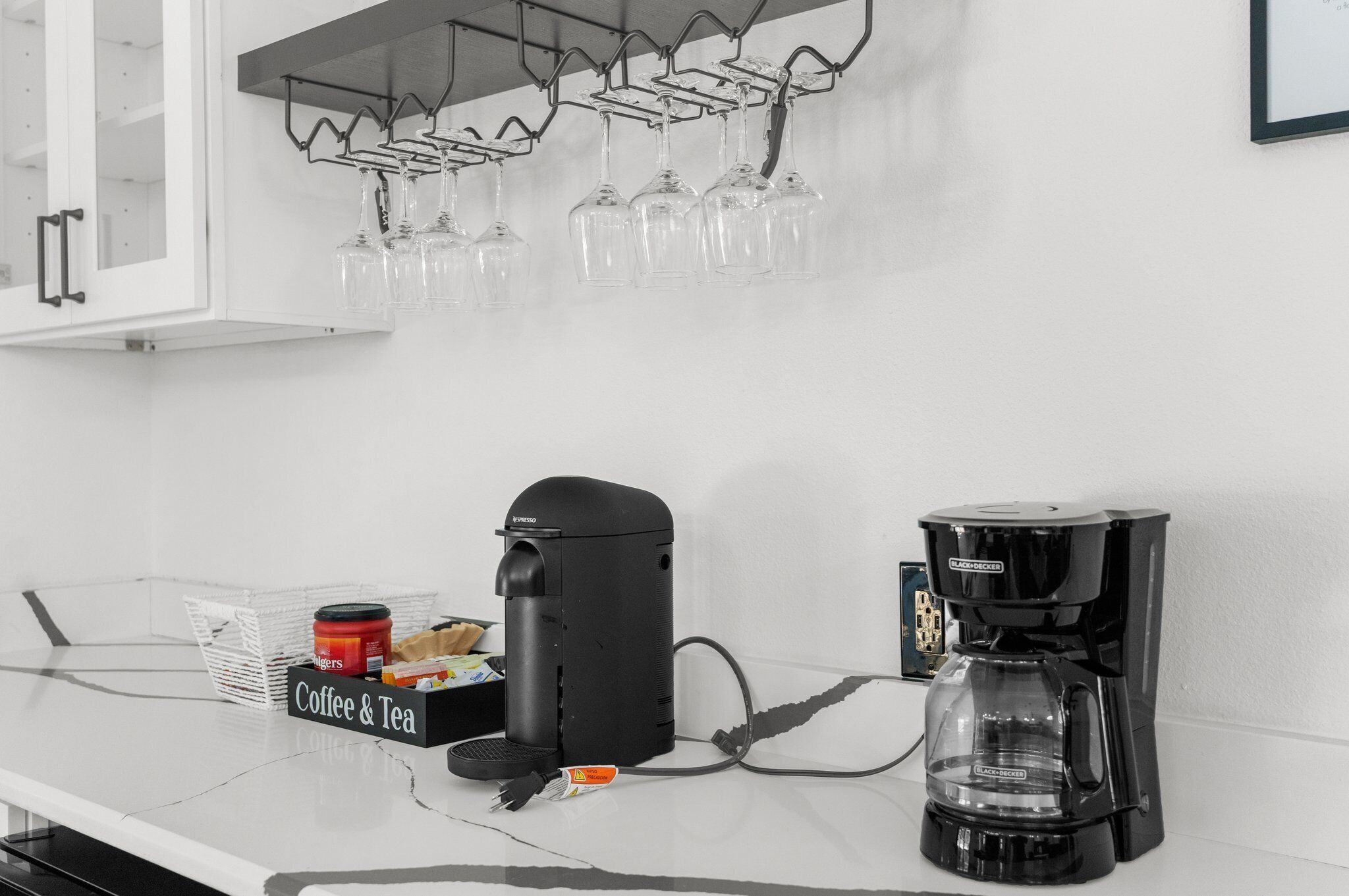 A kitchen with a coffee station, including a coffee maker and a coffee pot, and a wine rack with glasses.