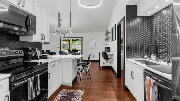 A modern kitchen with white cabinetry, black appliances, and a central island with bar stools. - Adventure Coast Modern; 3/3 Pool w/ Firepit, Fenced, Heated Pool (Spring Hill)