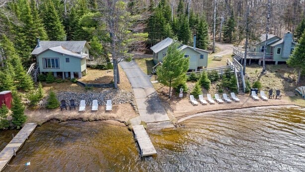 Ein Ferienhauskomplex am See mit mehreren Gebäuden, einem Steg und einer Reihe von Liegestühlen.