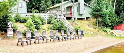 Een rij houten stoelen op een zanderig strand, met een houten trap die naar een hutje leidt.