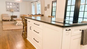 A spacious kitchen with white cabinetry, a black countertop, and a large window. - Luxury SouthPark Villa • 3BR • Spa Tub • Chef’s Kitchen • Near Dining & Uptown (Charlotte)