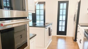 A modern kitchen with stainless steel appliances, white cabinetry, and a wooden floor. - Luxury SouthPark Villa • 3BR • Spa Tub • Chef’s Kitchen • Near Dining & Uptown (Charlotte)