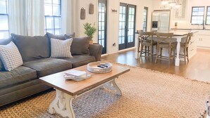 A living room with a sofa, coffee table, and dining area with chairs and a table. - Luxury SouthPark Villa • 3BR • Spa Tub • Chef’s Kitchen • Near Dining & Uptown (Charlotte)