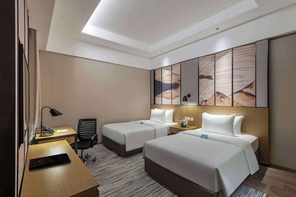 A hotel room with two beds, a desk, a chair, and a large window.