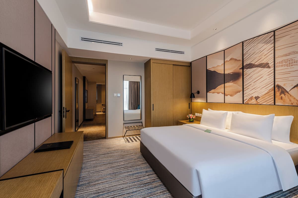 A modern hotel room with a large bed, a flat-screen TV, a desk, and a walk-in closet.