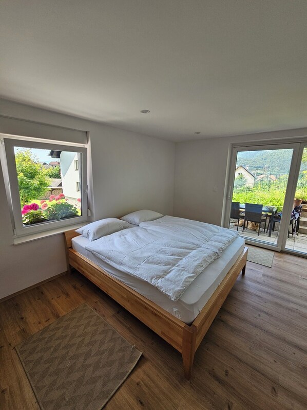 Une chambre avec un lit en bois, de grandes fenêtres et une vue sur un jardin et des montagnes.