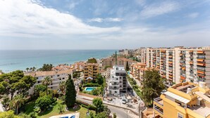A coastal cityscape with a mix of residential buildings, a clear sky, and a view of the sea. - Coastal Charm: Renovated 2-Bed Apt, Pool, Sea Views REF056 (Benalmádena)
