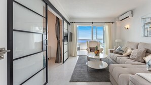 A modern living room with a sofa, coffee table, and a view of the sea. - Coastal Charm: Renovated 2-Bed Apt, Pool, Sea Views REF056 (Benalmádena)