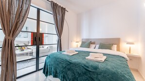 A modern bedroom with a large bed, two bedside lamps, and a view through a glass door. - Coastal Charm: Renovated 2-Bed Apt, Pool, Sea Views REF056 (Benalmádena)