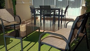 An outdoor patio with a glass table and chairs, surrounded by artificial grass, and a large window with a view of the outdoors. - Charmant 2 Pièces Avec Jardinet (les issambres)