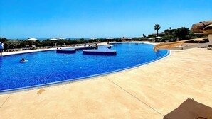 A large outdoor swimming pool with a clear blue sky, surrounded by lounge chairs and umbrellas. - Charmant 2 Pièces Avec Jardinet (les issambres)