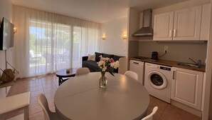 A modern kitchen with a dining area, a washing machine, and a large window with curtains. - Charmant 2 Pièces Avec Jardinet (les issambres)