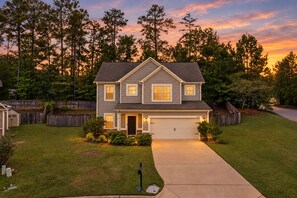 A two-story residential house with a garage, surrounded by a well-maintained lawn and trees. - Fire Pit, Central to RTJ, Downtown Auburn & Opelika - Sleeps 12 (Opelika)