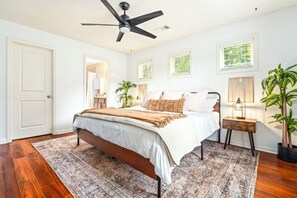 A bedroom with a bed, a nightstand, a ceiling fan, and a potted plant.
