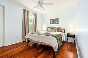 A bedroom with a bed, a ceiling fan, a nightstand, and a window with curtains. - Fire Pit, Central to RTJ, Downtown Auburn & Opelika - Sleeps 12 (Opelika)
